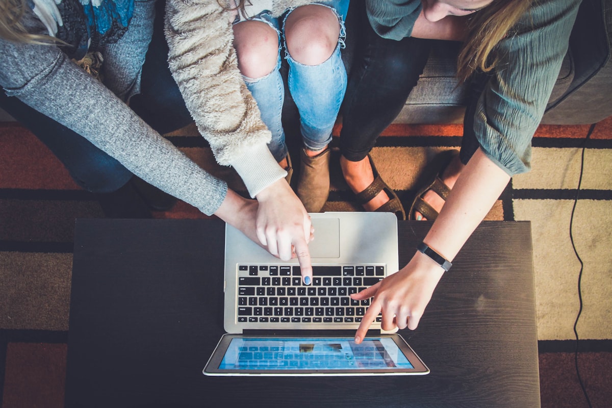 Person typing code prompts into AI chatbot on laptop with mobile phone showing app development